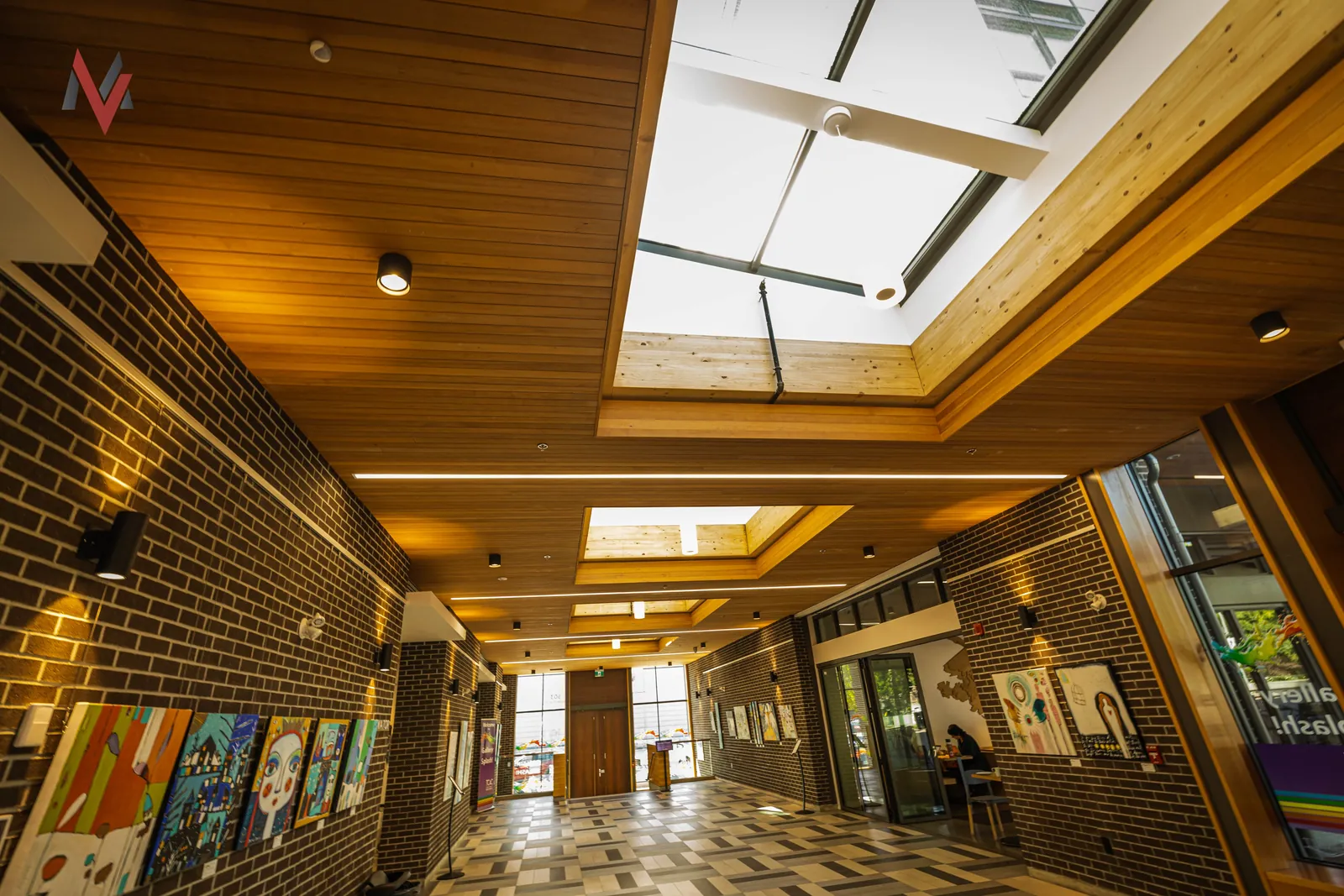 Brick-walled lobby with a wood slat ceiling, skylights and glazed entry doors in a BC community building, an MV Construction project