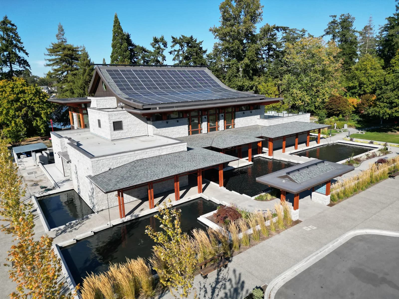 Modern stone building with solar panels and water feature — energy-efficient construction aligned with BC Step Code